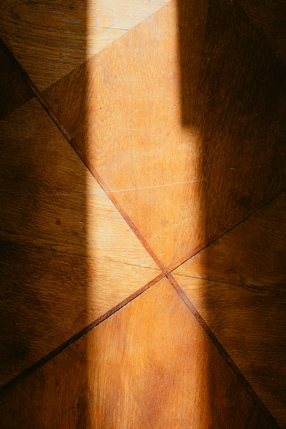 Geometrická drevená parketová podlaha s ostrou diagonálnou tieňou.